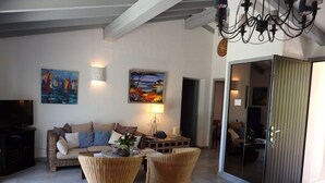 Una sala de estar con un sofá, dos sillones de mimbre, una mesa de centro, un televisor y obras de arte en las paredes.