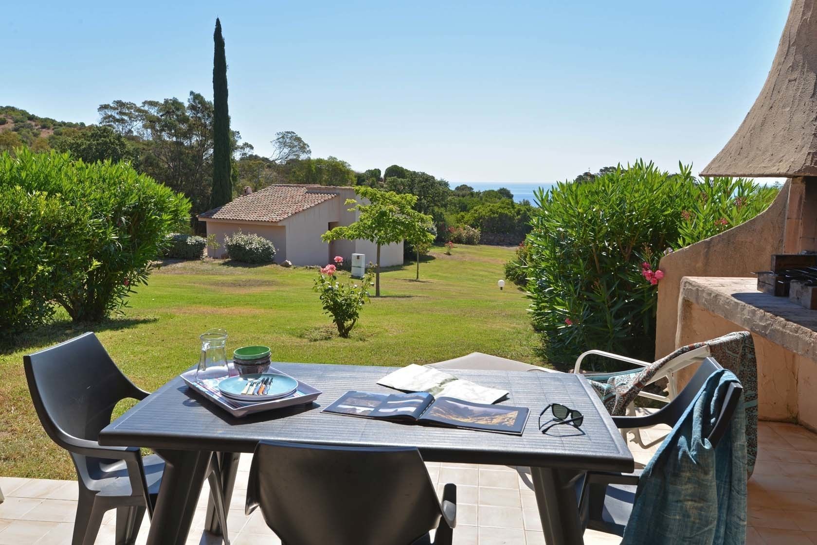 An outdoor patio with a table set for two, a chair, and a grill area.