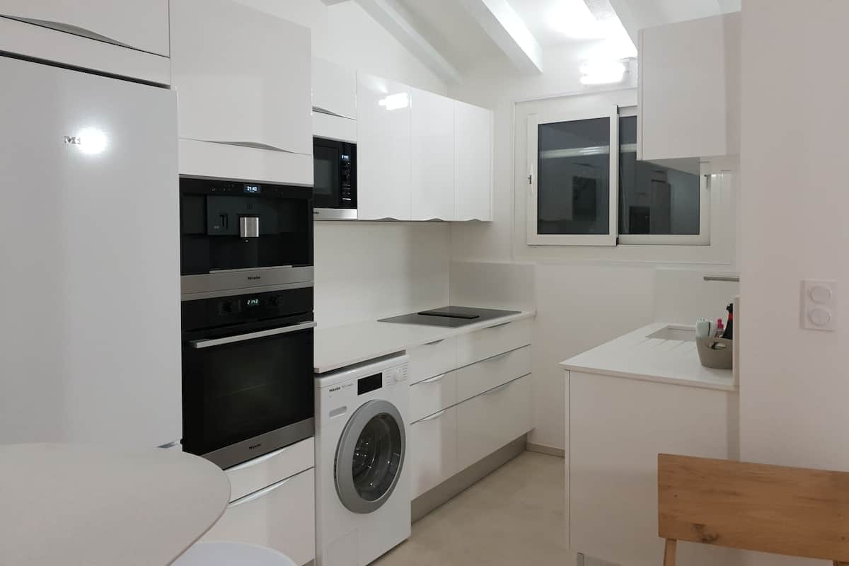 A modern kitchen with white cabinetry, a built-in oven, a microwave, and a washing machine.
