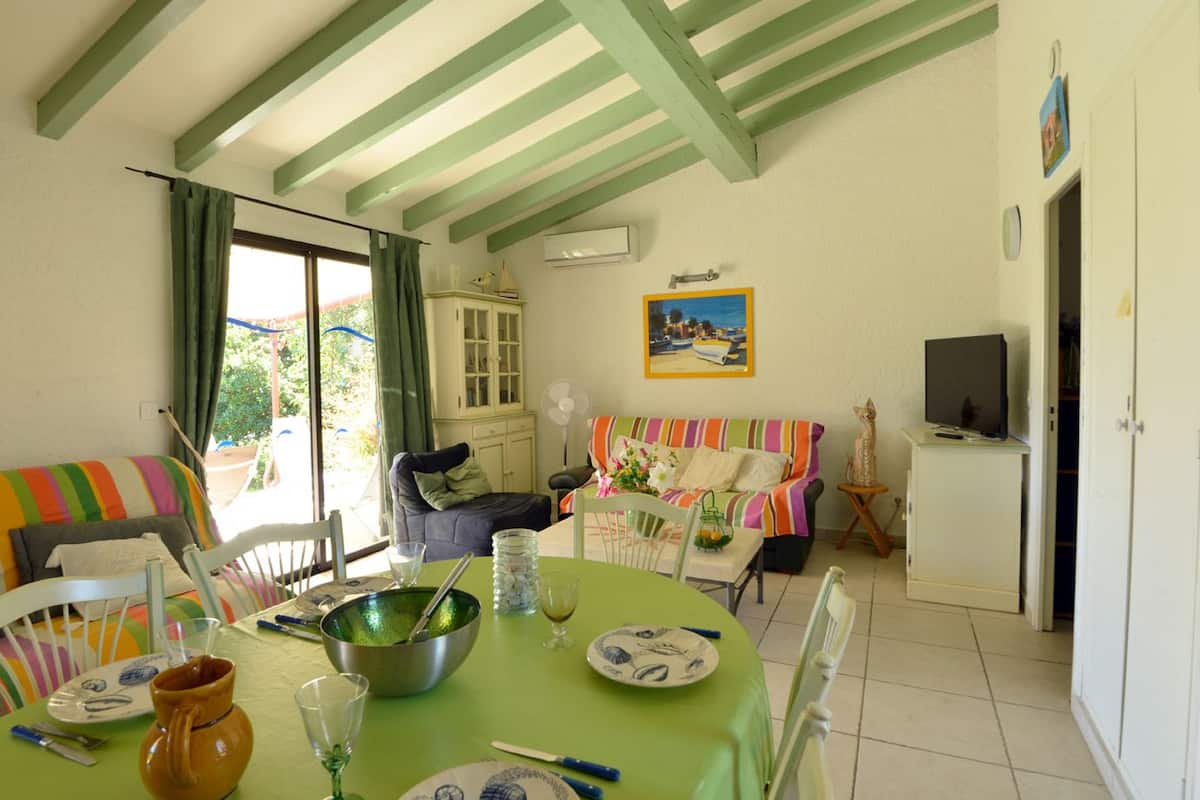 A dining area with a table set for two, a sofa, a cabinet, and a television.