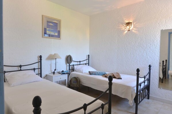 A room with two beds, a nightstand, a lamp, a hat, and a wall-mounted light fixture.