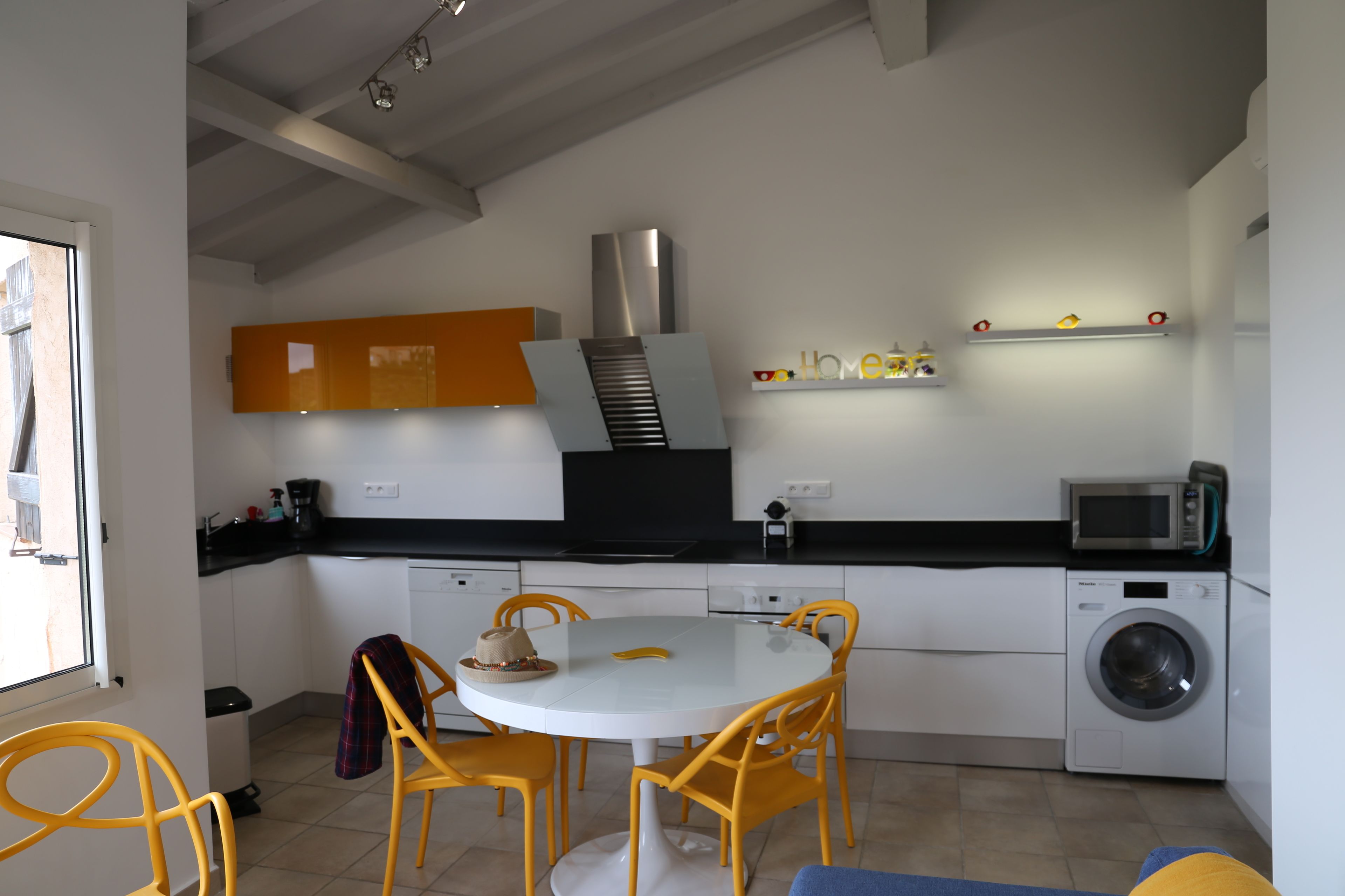 Una cocina moderna con una mesa redonda, sillas amarillas, una lavadora y un microondas.