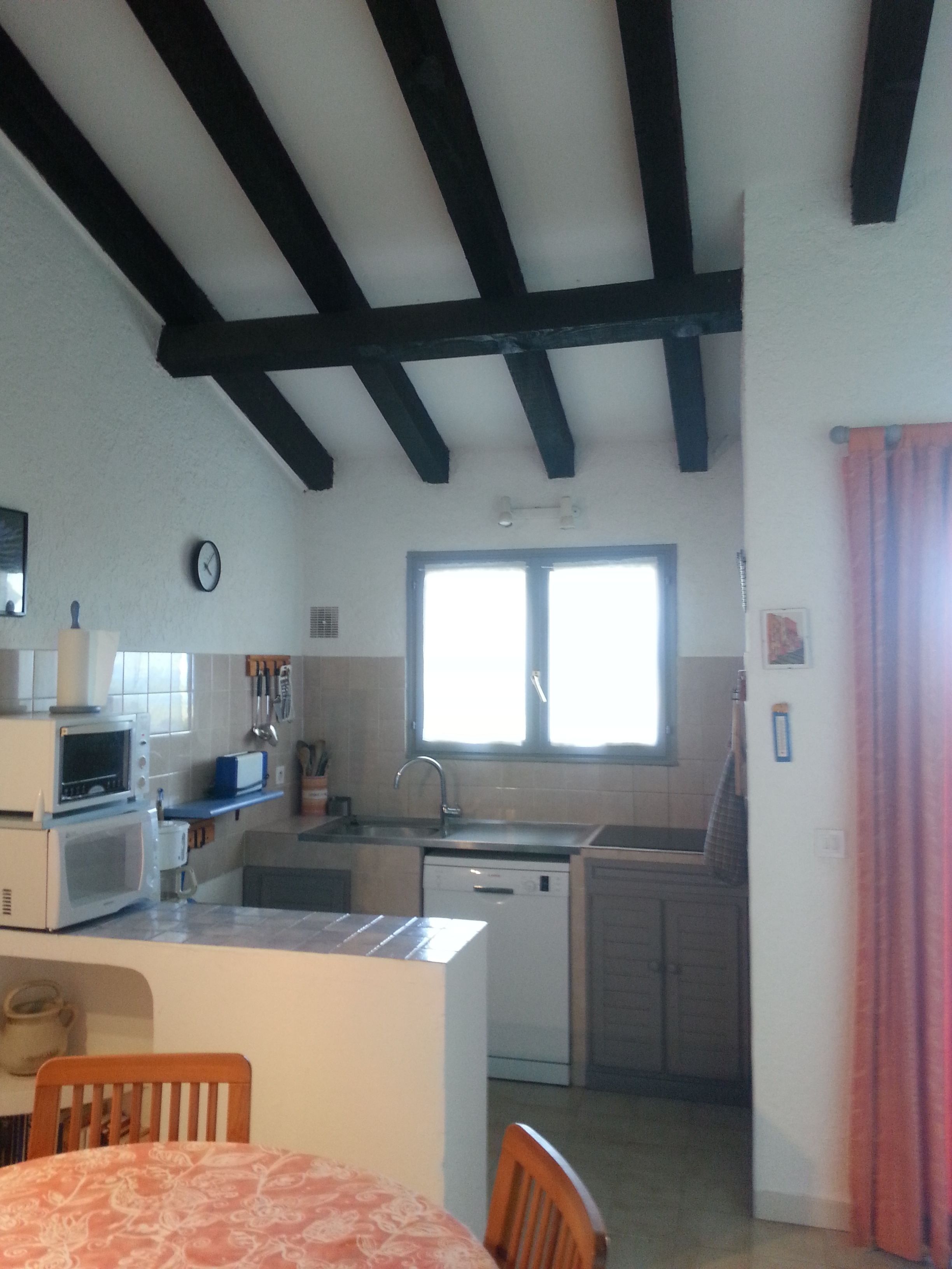 Angolo cottura compatto con zona pranzo, dotato di forno a microonde, tostarelle, lavello e finestra con tende.
