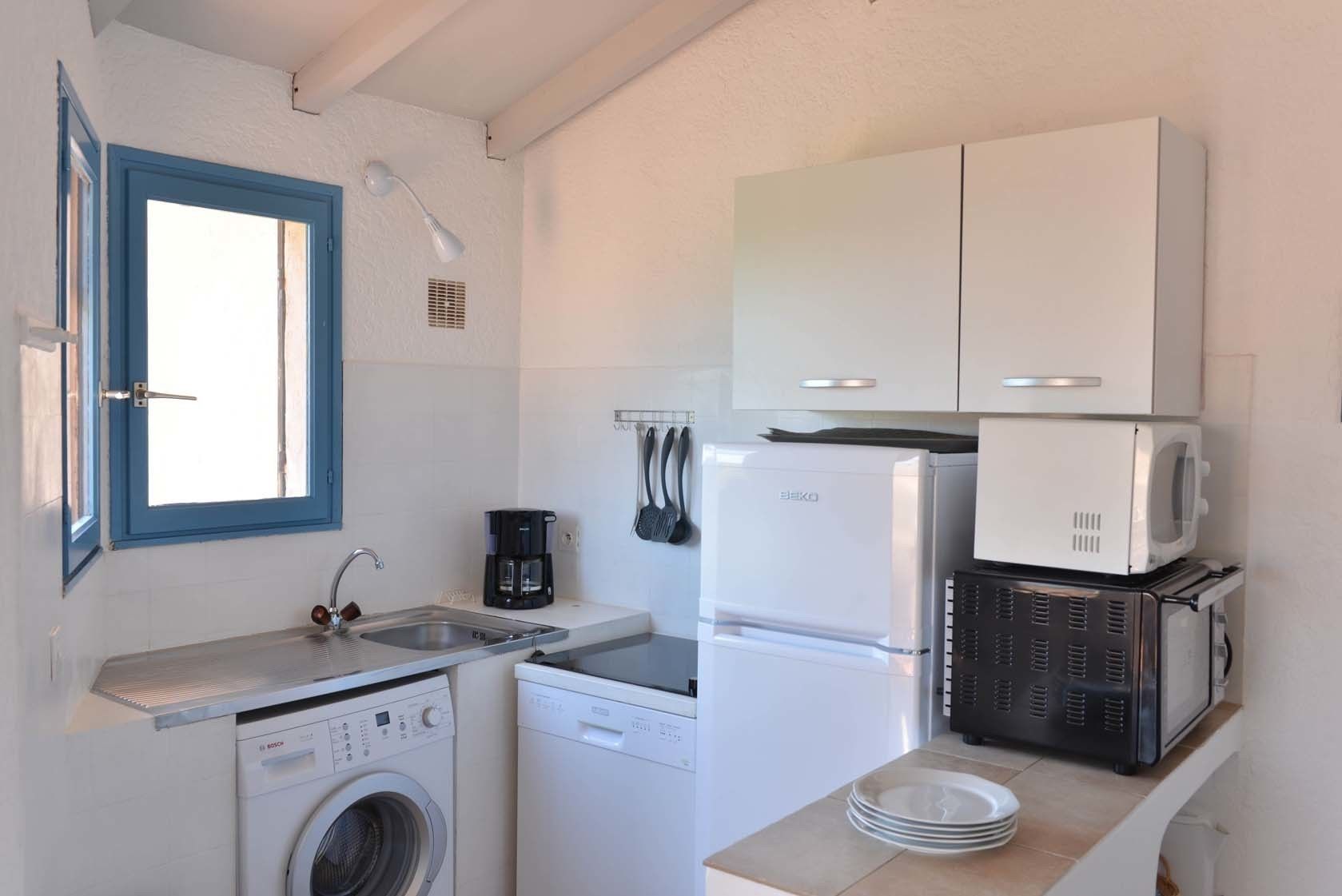 A compact kitchen with a washing machine, a coffee maker, a microwave, and a refrigerator.