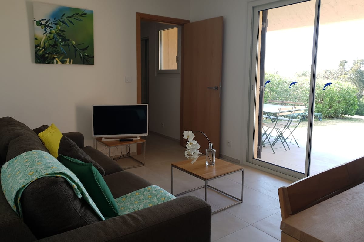 A living room with a sofa, a flat-screen TV, a small table, and a sliding glass door leading to an outdoor area.