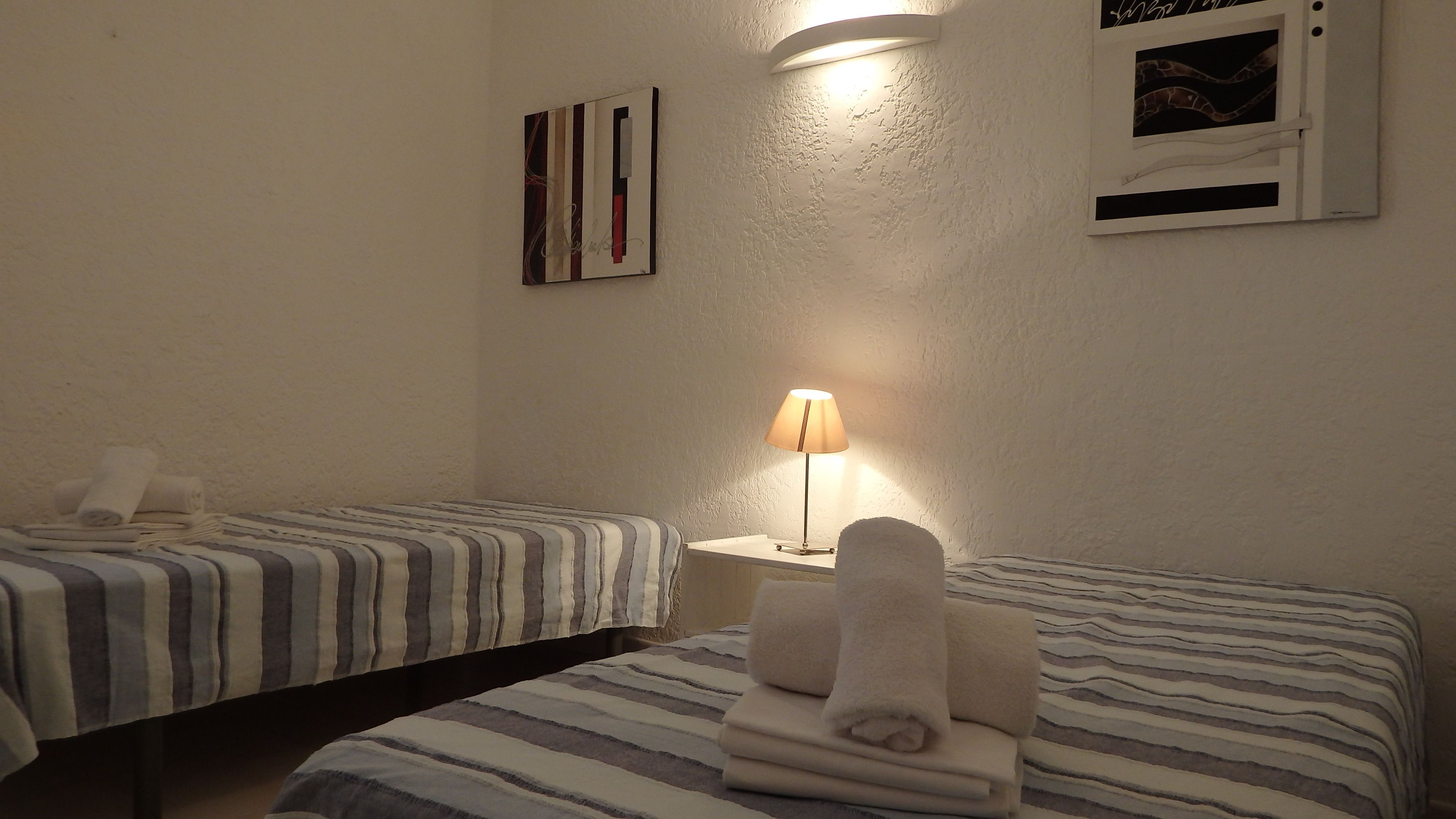 Et hotelværelse med to senge, begge med stribet sengetøj, et natbord med lampe og en billedramme på væggen.