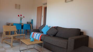 A living room with a sofa, a wooden chair, a small table, and a dining table with chairs.