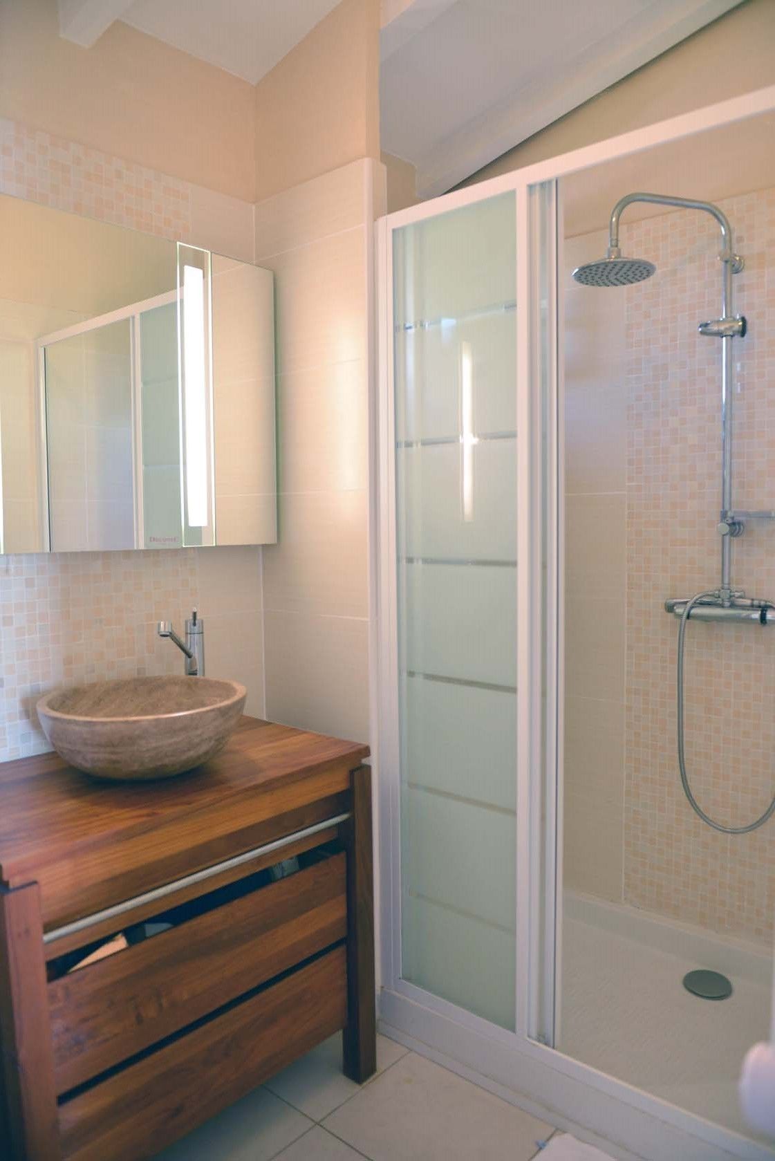 A bathroom with a wooden vanity, a large mirror, a glass shower enclosure, and a tiled shower wall.