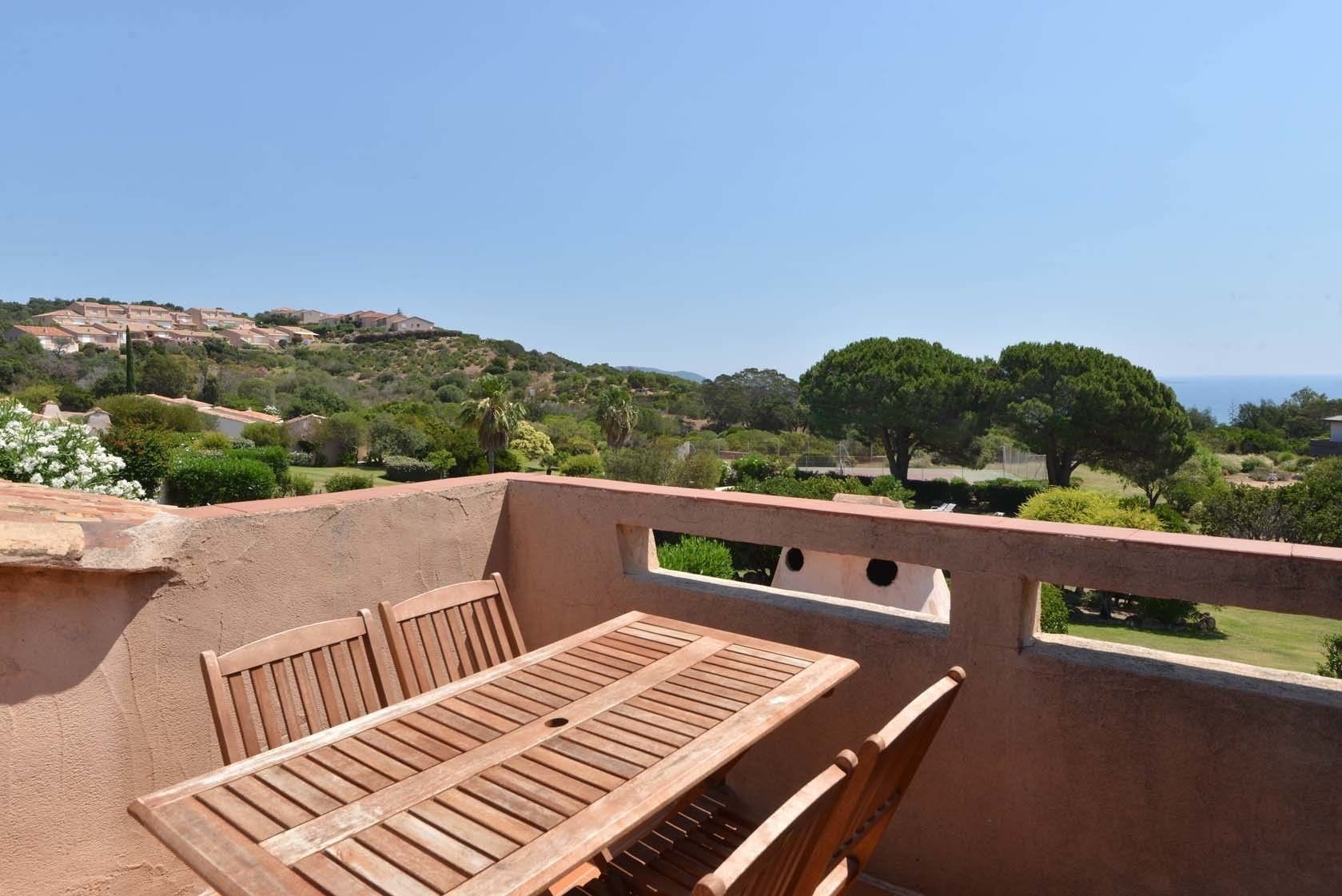 Una terraza con mesa y sillas de madera, con vistas a un paisaje pintoresco con colinas y árboles.