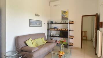 A living room with a brown sofa, glass coffee table, and a bookshelf with decorative items.