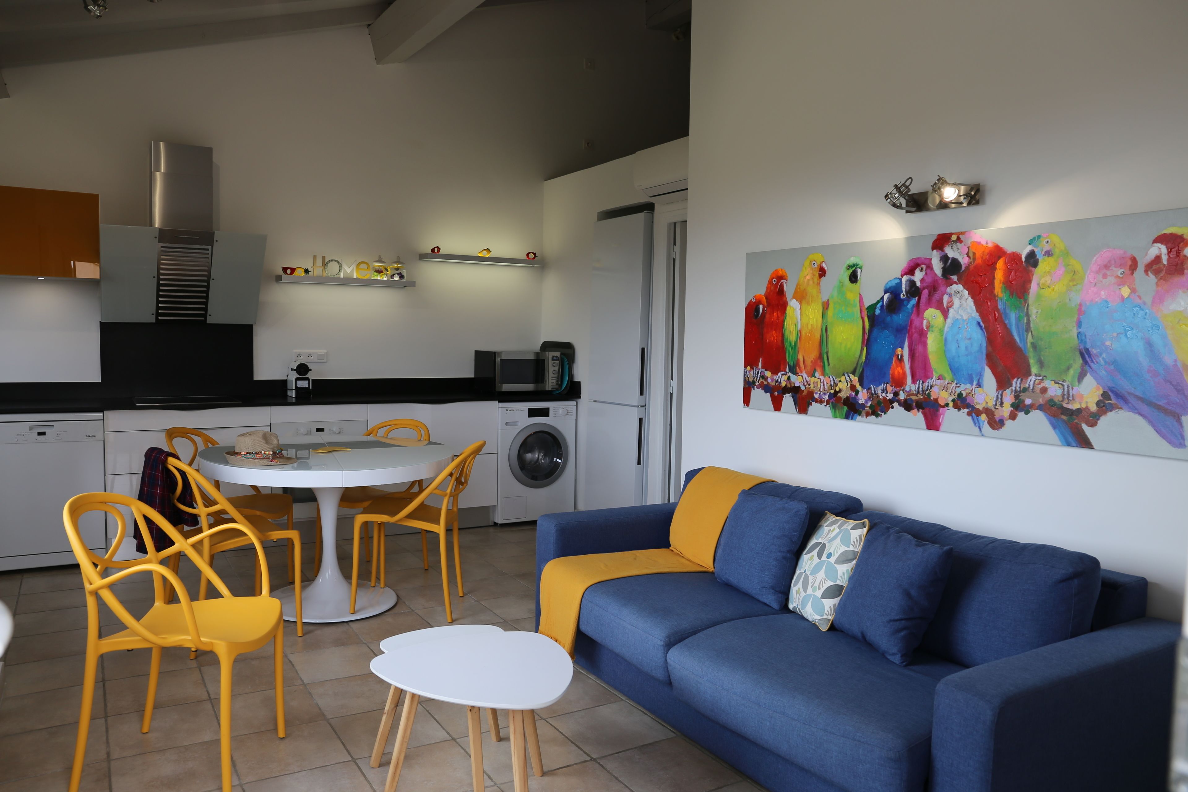Een moderne keuken met een eethoek, een bank en een kleurrijk schilderij van een papegaai.