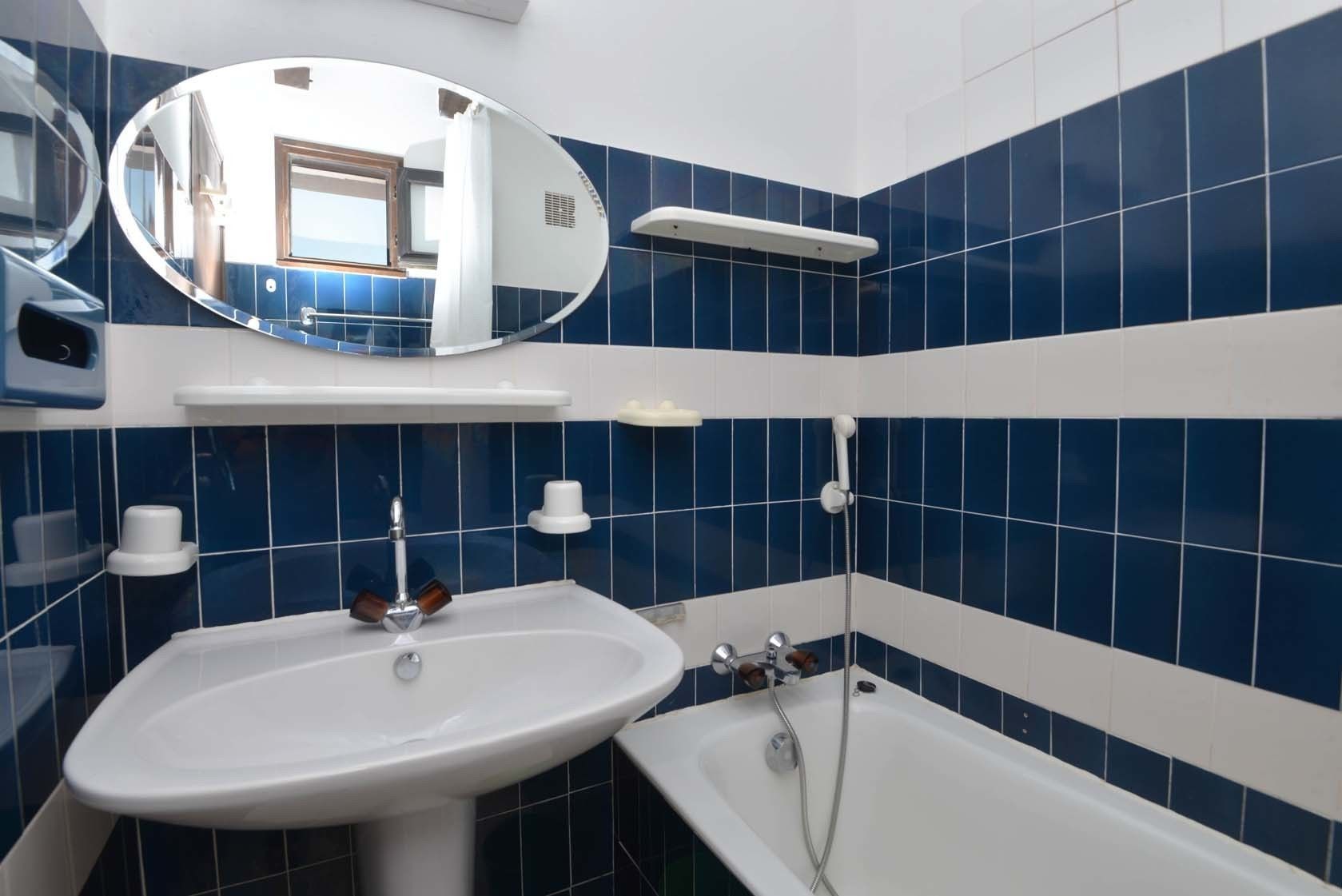 A bathroom with a white sink, a bathtub, and blue-tiled walls.