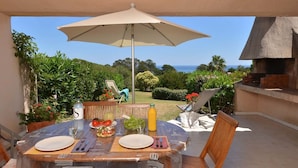 Un espacio de comedor al aire libre con mesa, sillas, sombrilla y vista al océano.