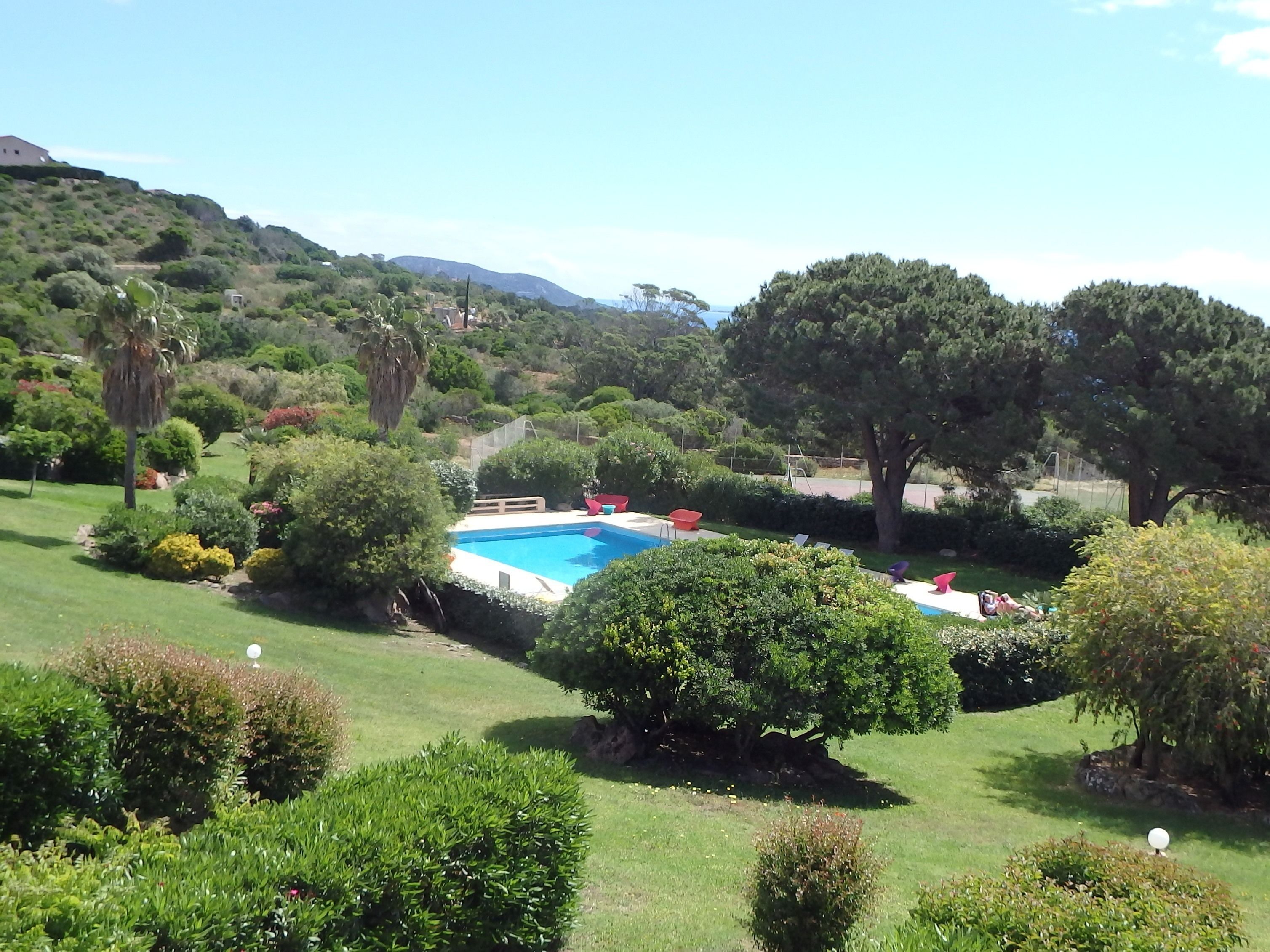 Piscina rodeada por vegetação exuberante e árvores, com vista desobstruída para uma paisagem montanhosa ao fundo.