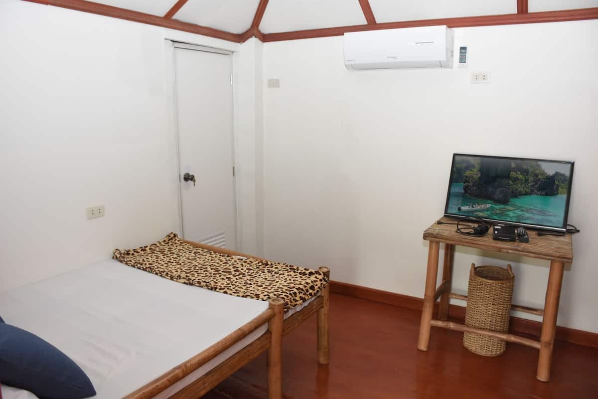 A small, simple room with a bed, a television on a wooden stand, and a door.