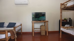 Ein Zimmer mit zwei Holzkohlenbetten, einem kleinen Tisch mit Fernseher und einer Wandklimaanlage.