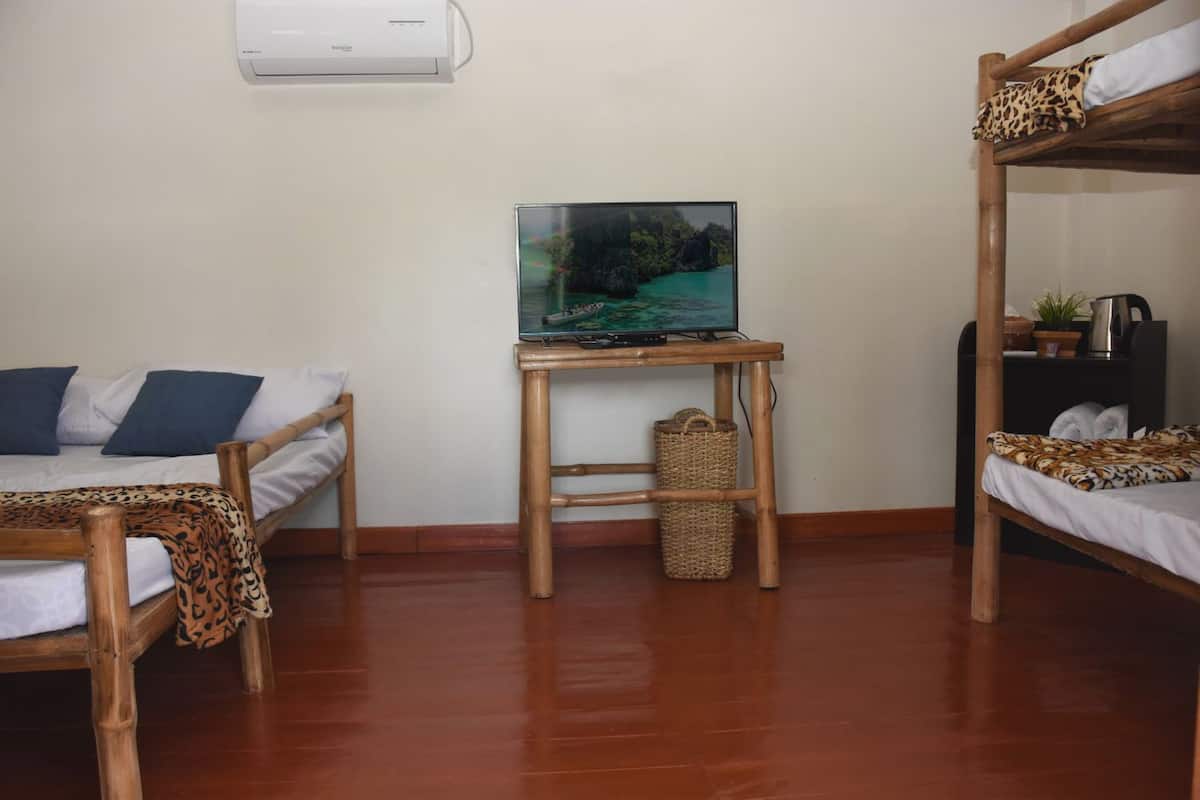 A room with two wooden bunk beds, a small table with a television, and a wall-mounted air conditioner.