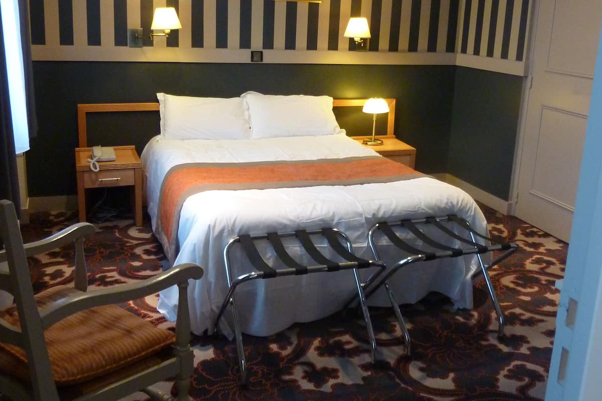 Ein Hotelzimmer mit einem Bett, zwei Nachttischlampen, einem Sessel, einem kleinen Tisch und einer Tür.