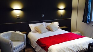 Een hotelkamer met een bed, een witte fauteuil en twee wandlampen.