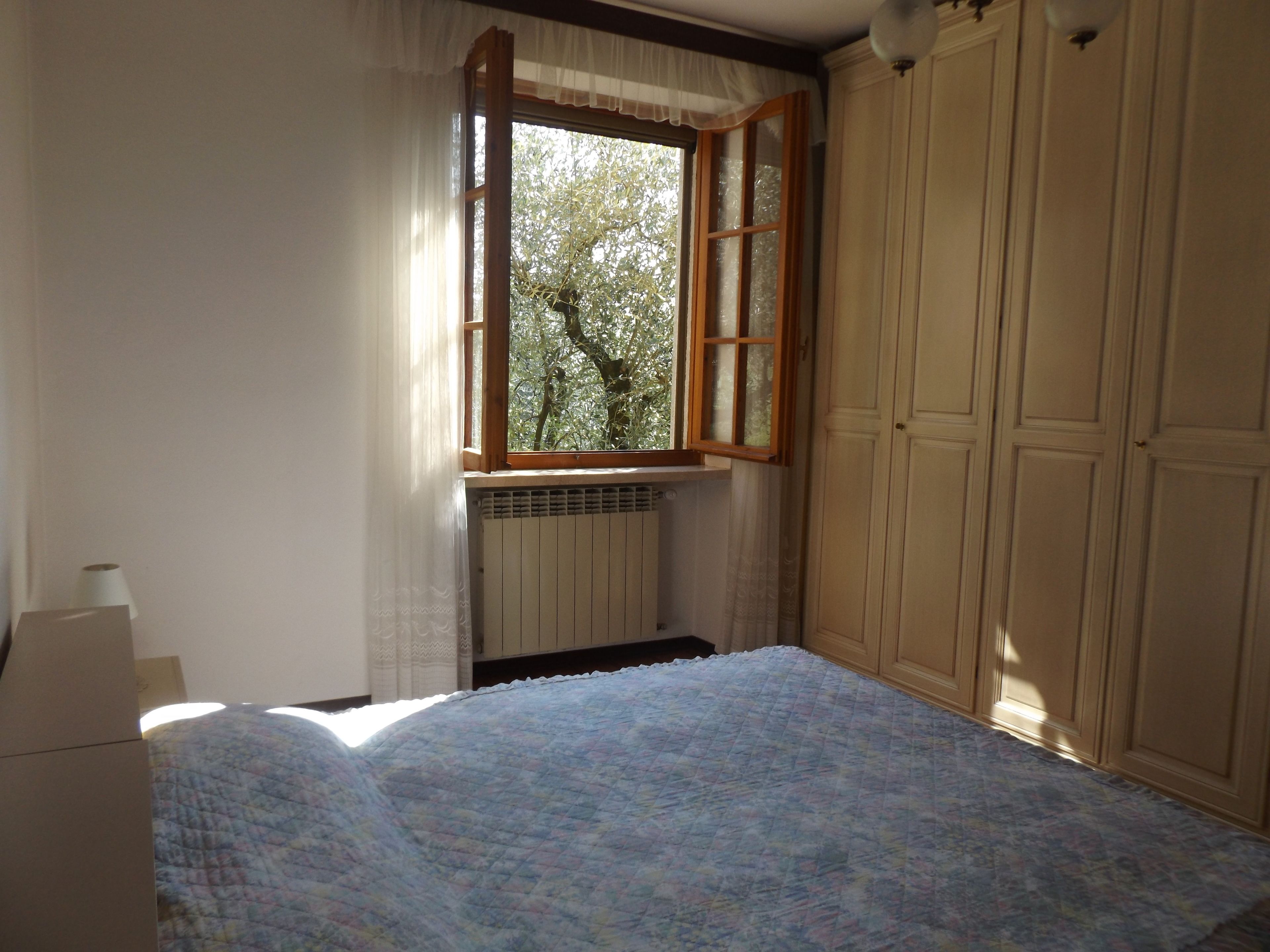 A bedroom with a bed, a radiator, a window with curtains, and a wardrobe.