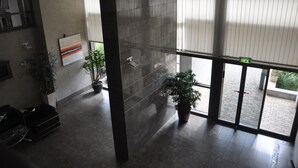 A lobby with a modern design, featuring a large glass door leading outside, potted plants, and a wall-mounted artwork.