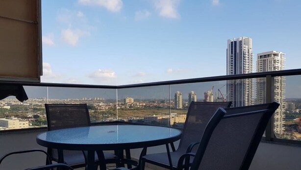 A round table with four chairs on a balcony with a city view.