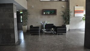 A lobby with a reception desk, two black sofas, a small table, and potted plants.