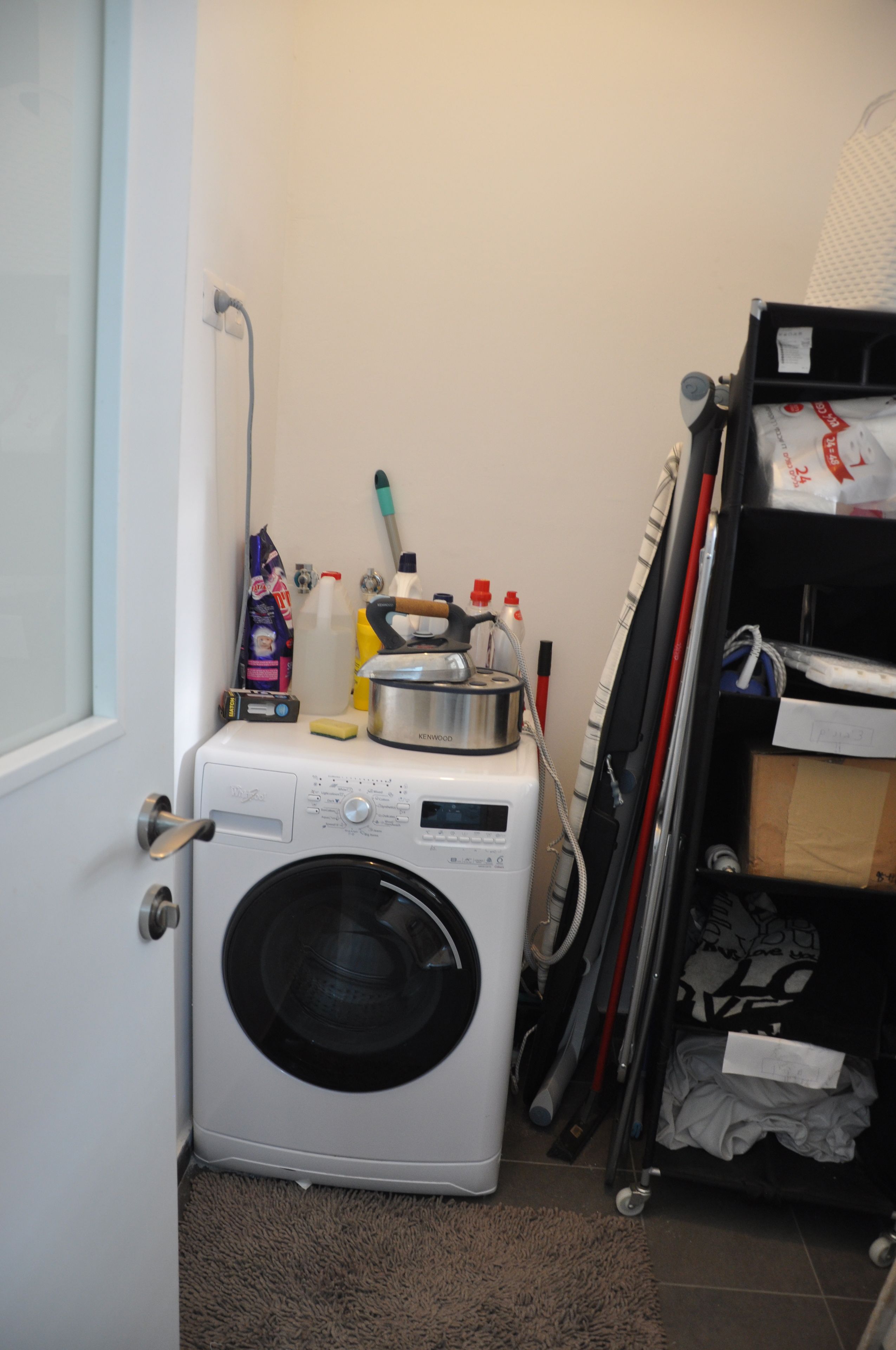 A compact laundry area with a washing machine, a drying rack, and various cleaning supplies.