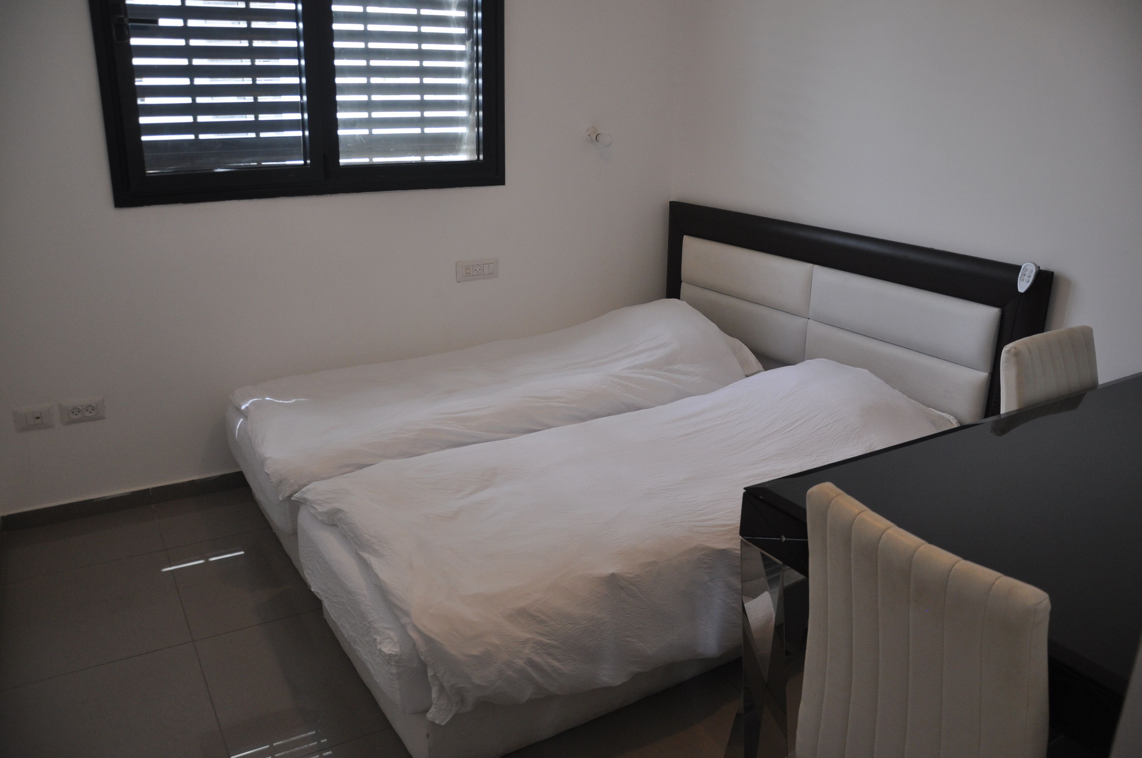 A small, clean room with a single bed, a chair, and a window with blinds.