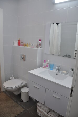 A bathroom with a toilet, sink, mirror, and shelves with toiletries. - Isra Home Yitshak Sadeh 6 Apartment (Bat Yam)