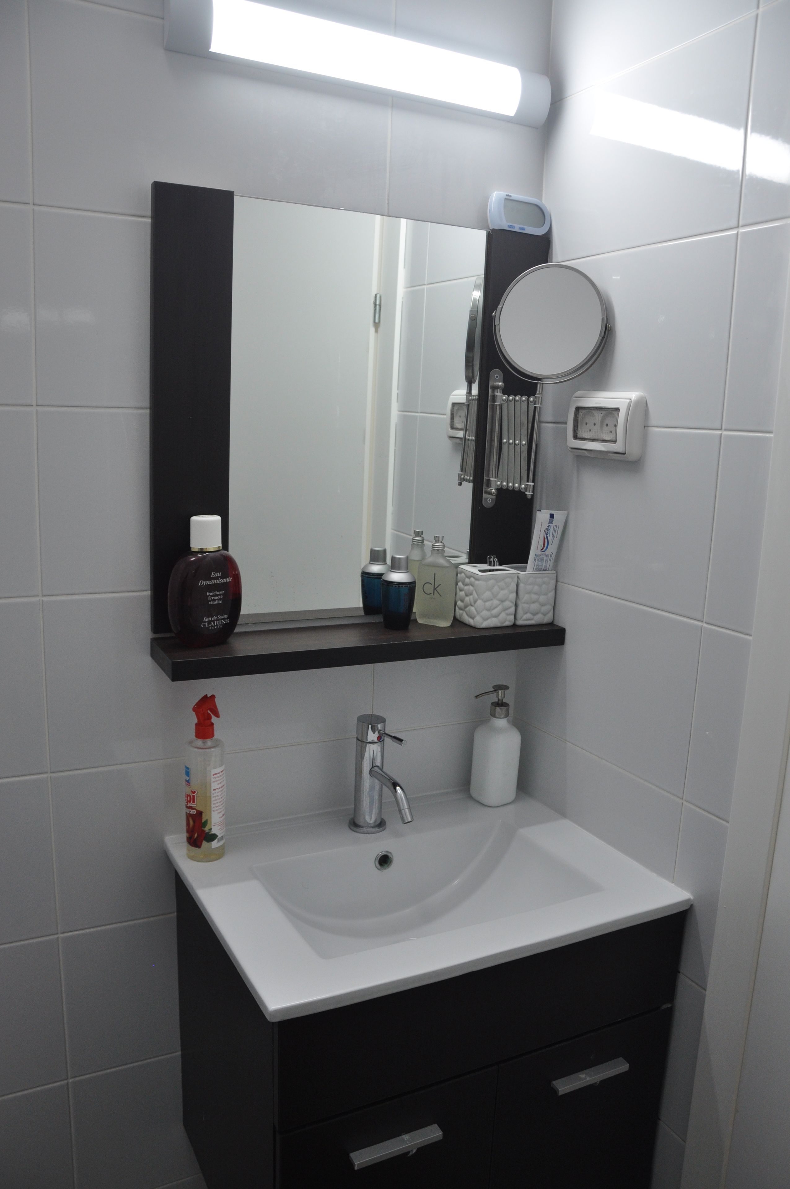 A bathroom with a white sink, black cabinet, and a mirror above it. There are toiletries on the sink and a soap dispenser on the cabinet.