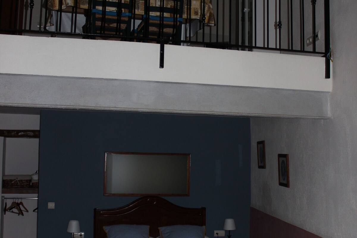 Een slaapkamer met een bed, nachtkastje, dressoir, raam en balkon met hekwerk.