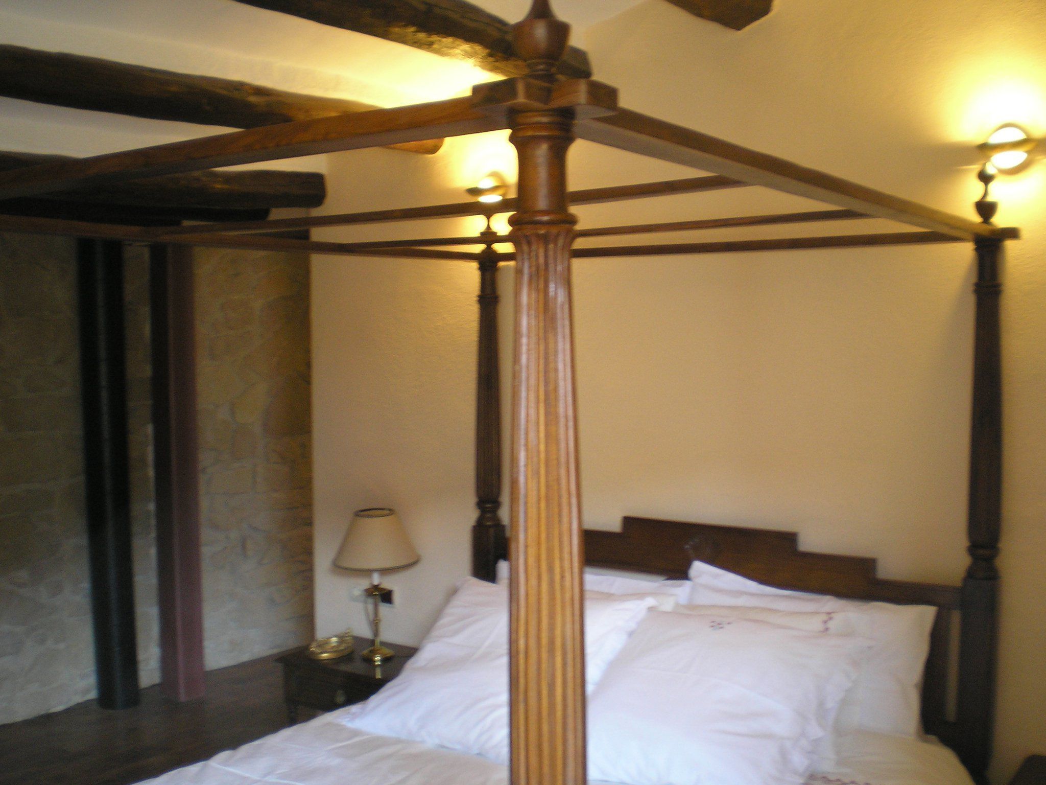 Una cama con dosel con ropa de cama blanca en una habitación con paredes de piedra y vigas de madera.