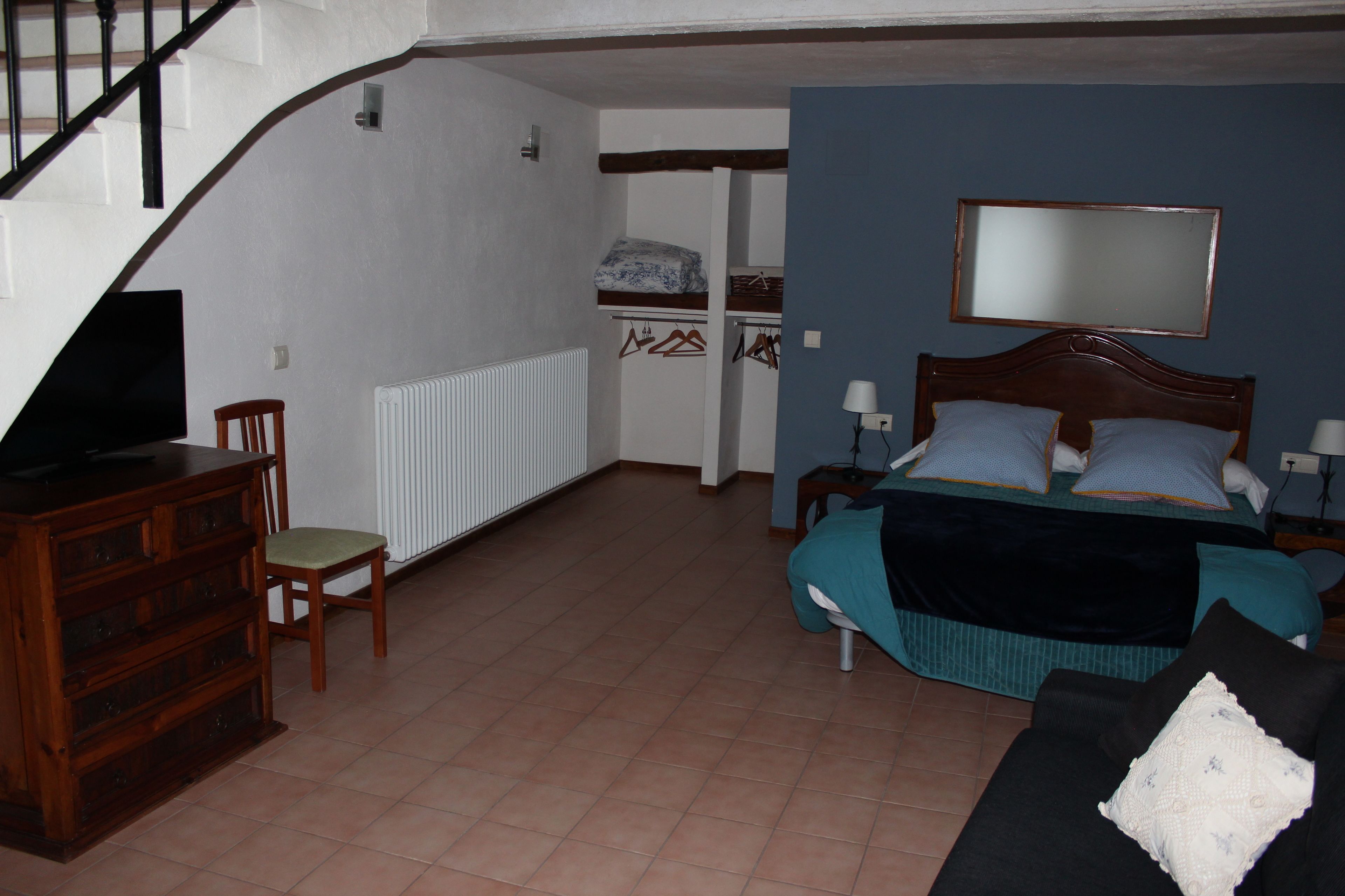 Une chambre à coucher comprenant un lit, une commode, une chaise, un miroir et un escalier.