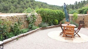 A patio with a round table and chairs, surrounded by a stone wall and lush greenery. - Ca L'Estruch (Vallclara)