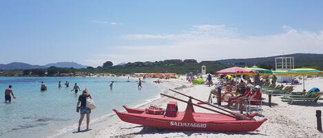 Una playa con aguas cristalinas, una torre de salvavidas y un bote rojo con la leyenda 'SALVATAGGIO'.