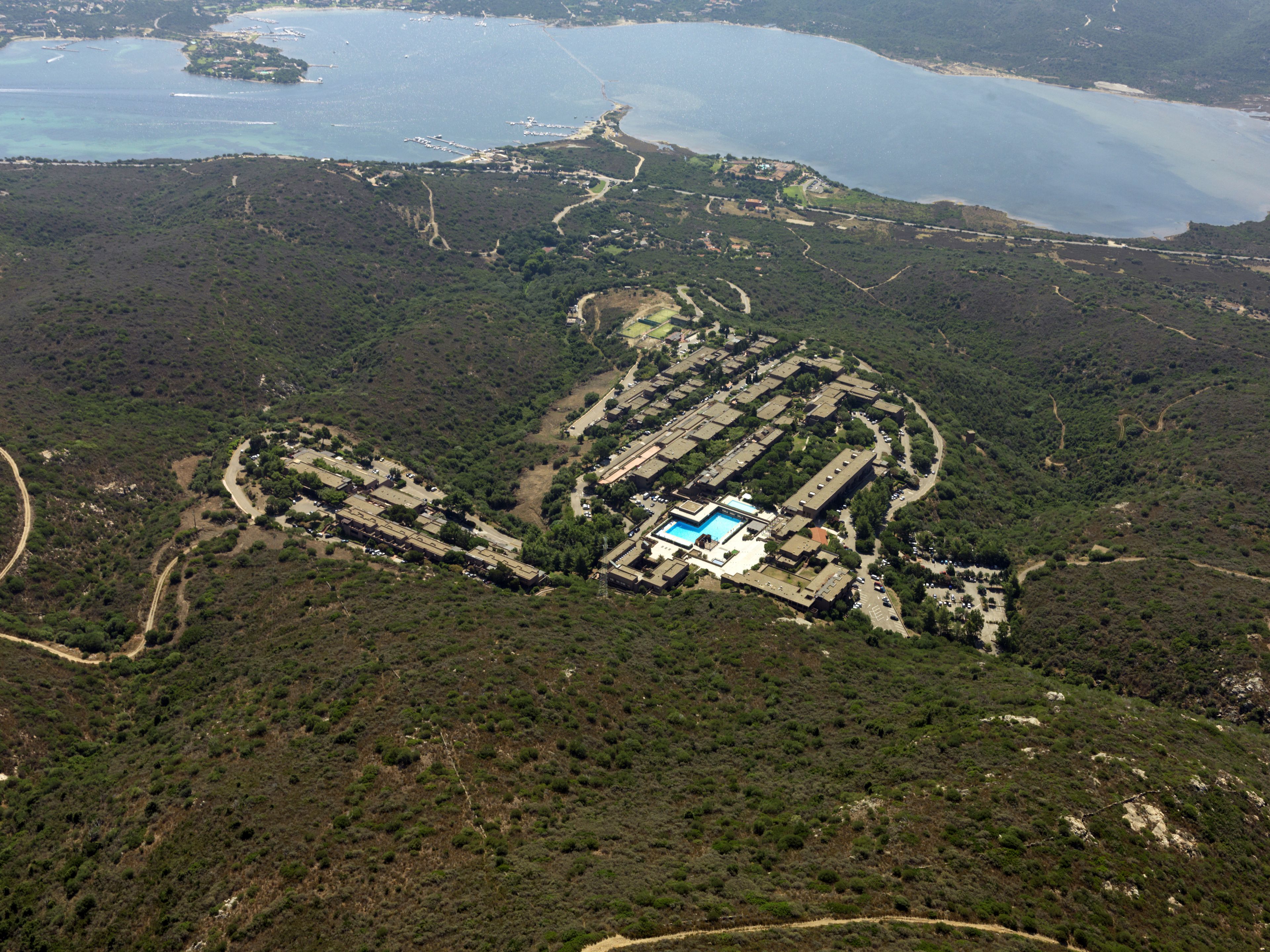 Vista aérea de un complejo turístico con una piscina central, rodeado por un bosque denso y una costa.