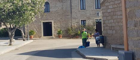 A stone building with a cross on top, a tiled roof, and a paved courtyard.