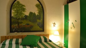 Una habitación con una cama con ropa de cama verde y blanca a rayas, un amplio ventanal con un cuadro de paisaje, una lámpara de noche y un armario verde.
