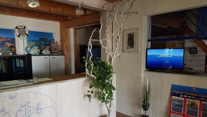 Un área de recepción con mostrador de madera, planta colgante, televisor montado en la pared y un cartel que anuncia vino sardo.