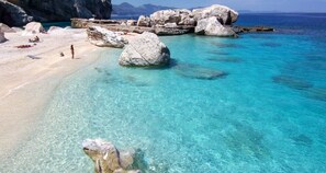 Uma praia com águas azul-turquesa cristalinas, grandes rochas e areal arenoso.