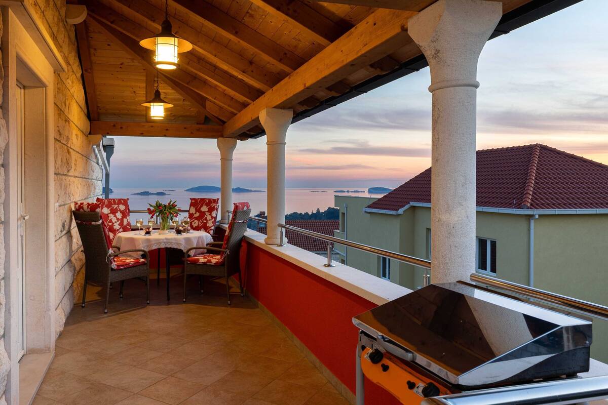 A covered outdoor dining area with a grill, red and white tablecloths, and a view of the sea.