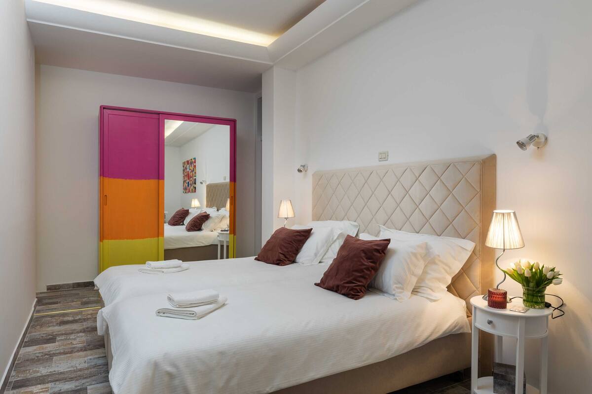 A hotel room with a bed, bedside lamps, a nightstand, and a mirror.