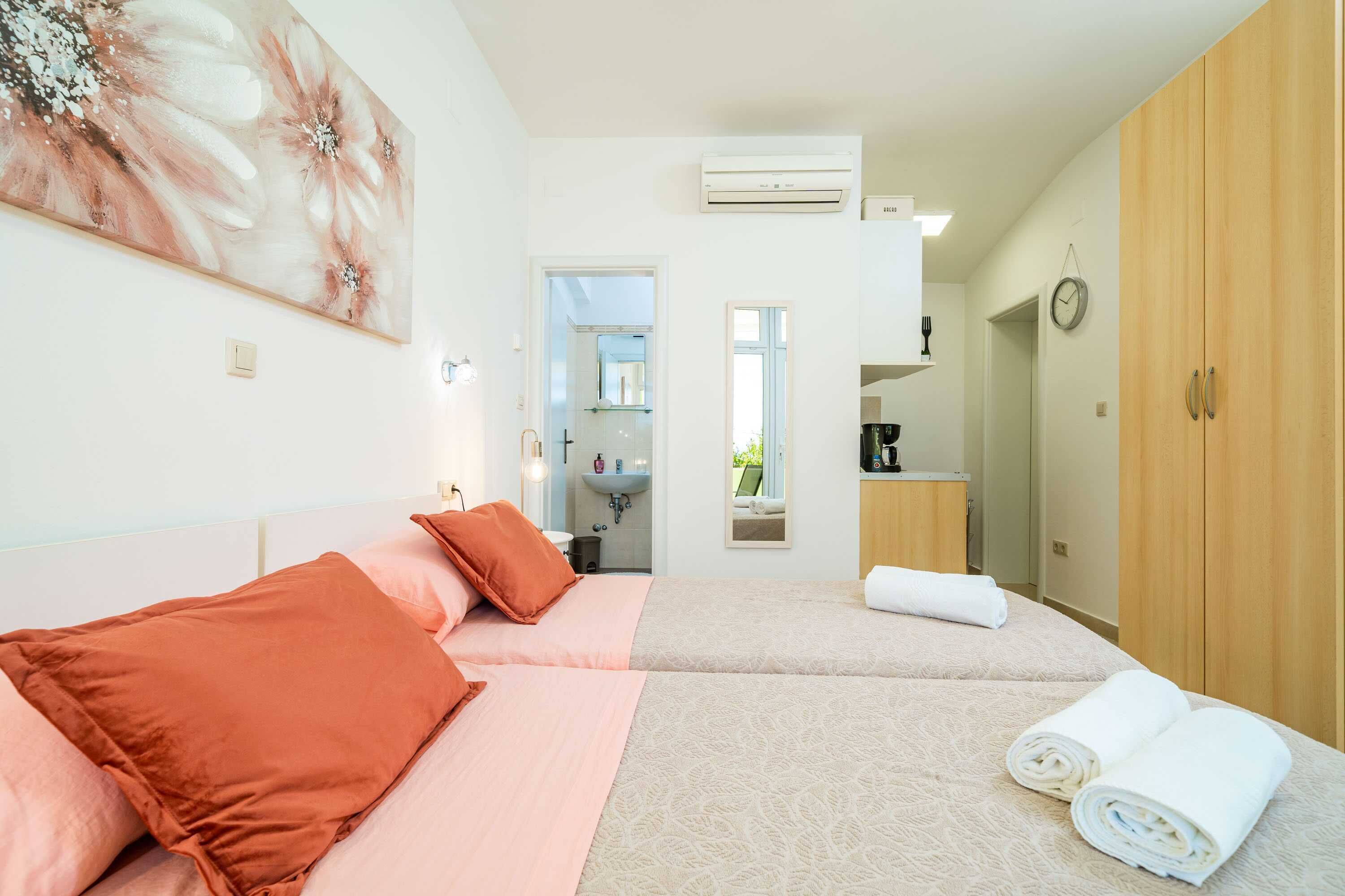 Quarto de hotel com duas camas, banheiro e cozinha compacta.