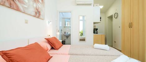 Quarto de hotel com duas camas, banheiro e cozinha compacta.