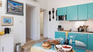 A modern kitchen with teal cabinets, a glass table, and various food items. - Apartments Subrenum (Zupa dubrovacka)