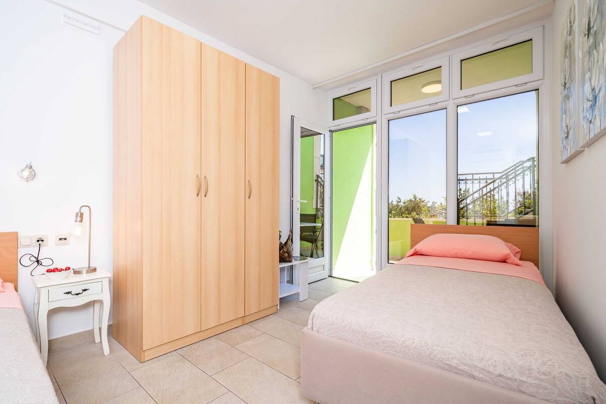 A bedroom with a bed, a wardrobe, a desk with a lamp, and a window with a view of a balcony.