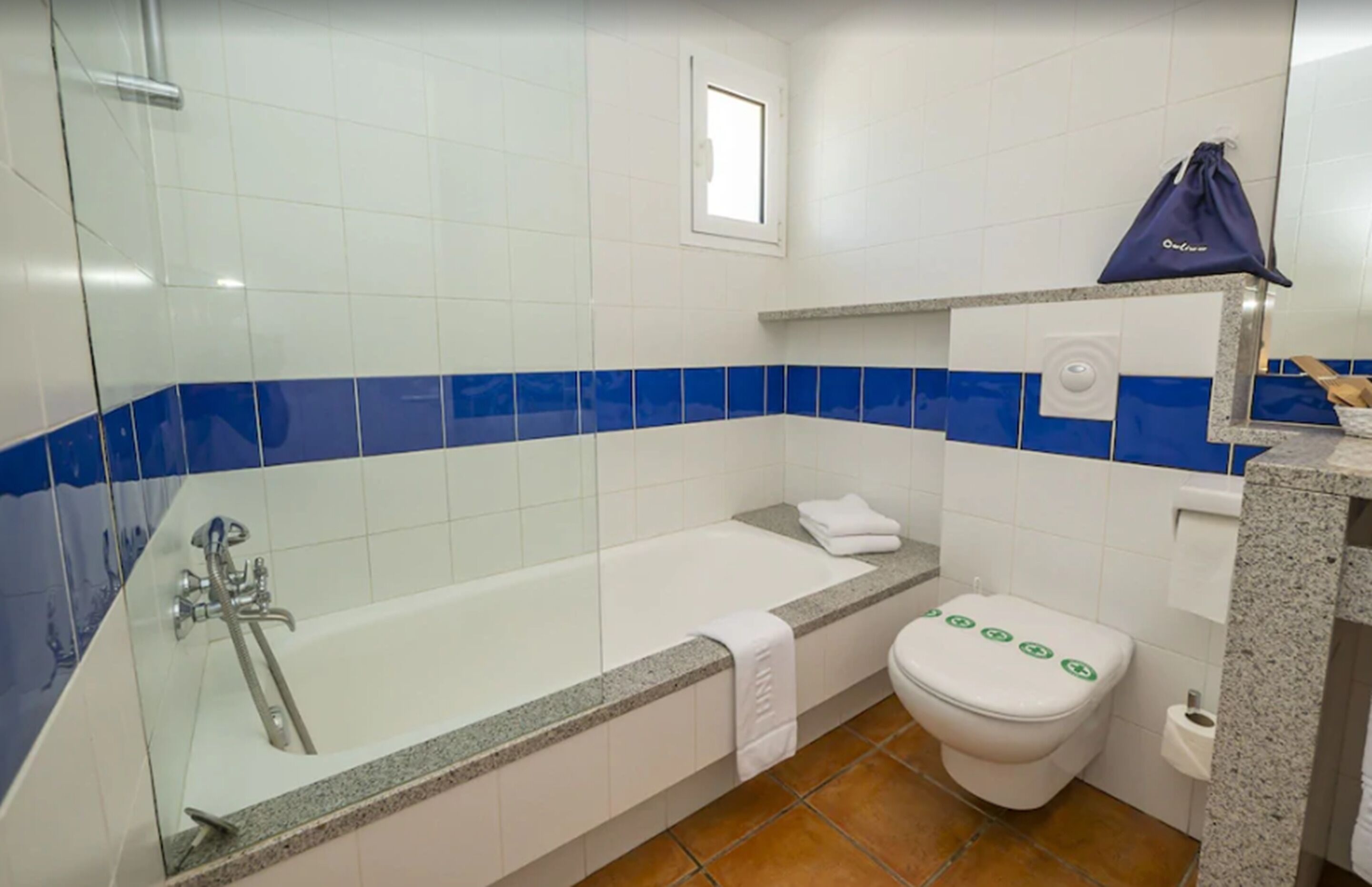 A bathroom with a glass-enclosed bathtub, a white toilet, and blue-tiled walls.
