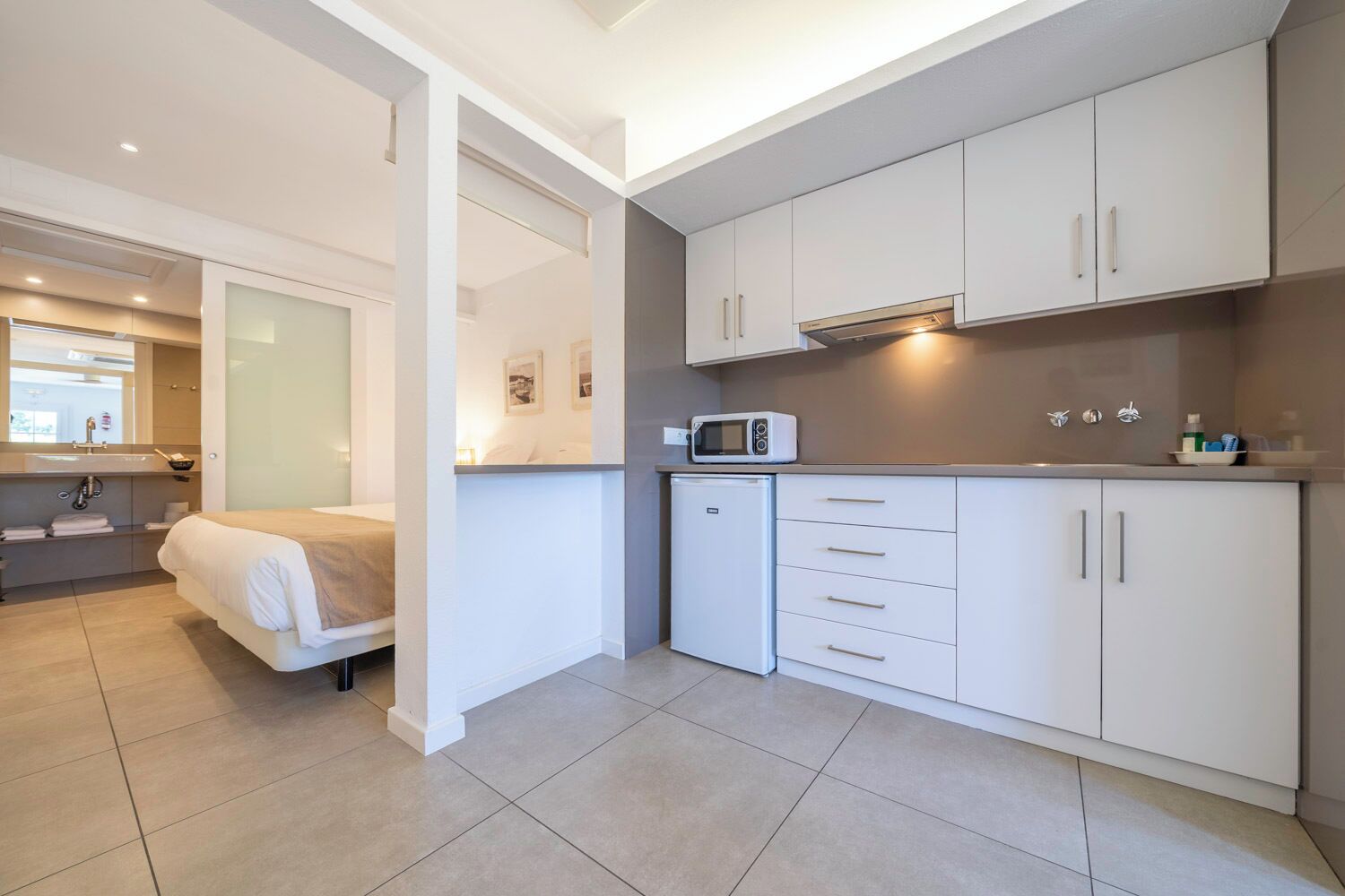 Camera d'albergo compatta con angolo cottura, un letto, bagno con specchio e una piccola zona salotto.