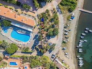 An aerial view of a resort with a swimming pool, beach, and boats. - Hotel Calina (Cadaqués)